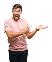 Wall Mural - Young handsome man over isolated background amazed and smiling to the camera while presenting with hand and pointing with finger.