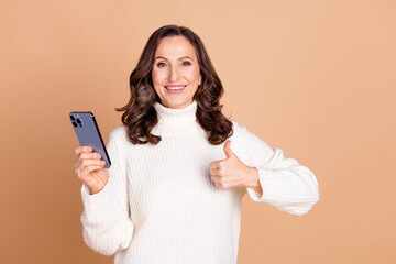 Canvas Print - Photo of lovely cheerful senior woman wear white stylish clothes hold gadget thumb up isolated on beige color background