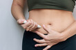 © Марина Демешко - Young woman putting a hormonal injection in her stomach with pen syringe on a grey background. The use of lipolytics in cosmetology. Preparations for figure correction. Insulin injections for diabetes