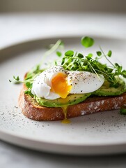 Wall Mural - A slice of toasted bread topped with avocado, poached egg, and microgreens.