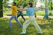© pressmaster - Mature female yoga trainer in activewear standing in front of several people repeating physical exercise after her in park