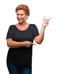 Atrractive senior caucasian redhead woman over isolated background with a big smile on face, pointing with hand and finger to the side looking at the camera.