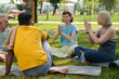 © pressmaster - Two mature women keeping their hands put together while sitting on mats in front of intercultural elderly men and showing new exercise