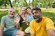 © pressmaster - Bearded multiethnic man taking selfie with group of active mature people waving hands and looking at smartphone camera outdoors