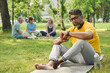 © pressmaster - Confident mature male trainer in yellow t-shirt and grey sweatpants looking at smartwatch while sitting on mat against restful people