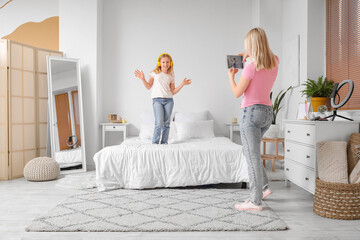 Wall Mural - Beautiful female blogger recording her daughter in headphones on tablet at home