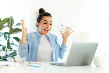 surprised happy indian or arabian successful business woman, sitting at a workplace, looking at a la