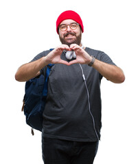 Wall Mural - Young hipster man wearing red wool cap and backpack over isolated background smiling in love showing heart symbol and shape with hands. Romantic concept.