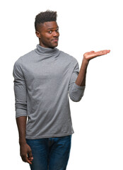 Wall Mural - Young african american man over isolated background smiling cheerful presenting and pointing with palm of hand looking at the camera.