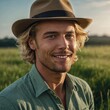 © Tamazina - Middle-aged Caucasian man with long blonde hair and beard, wearing tan cowboy hat and green button-up shirt, smiling in field