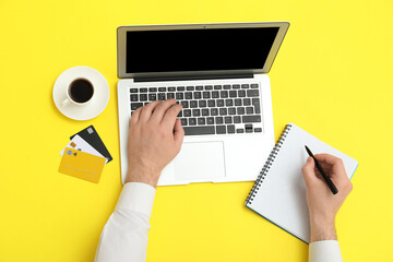Male hands with laptop, credit cards and cup of coffee on yellow background
