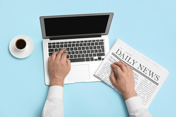 Wall Mural - Male hands with laptop, newspaper and cup of coffee on blue background