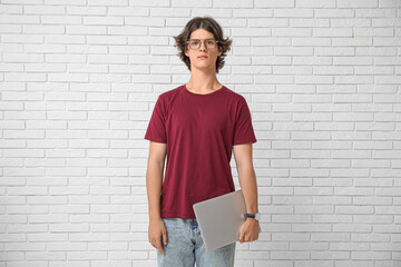 Male programmer in eyeglasses with laptop on white brick background