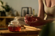 © pressmaster - Hands of tranquil woman in activewear holding glass of hot herbal tea over bamboo tray with teapot while enjoying break after training