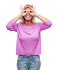 Wall Mural - Middle age blonde woman over isolated background doing ok gesture like binoculars sticking tongue out, eyes looking through fingers. Crazy expression.