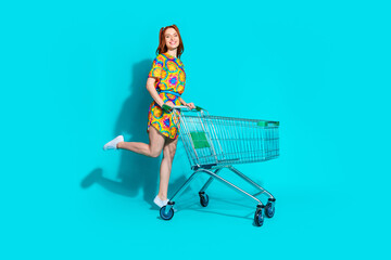 Canvas Print - Full size photo of pretty young girl walk push trolley wear trendy colorful outfit isolated on aquamarine color background