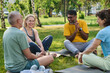 © pressmaster - Group of cheerful mature intercultural men and woman sitting on mats in front of female yoga instructor and having fun during chat