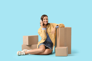 Beautiful young happy woman with parcels talking by mobile phone on blue background