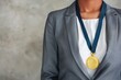 © Vilaysack - Close-up of a businesswoman in a grey suit wearing a gold medal on a blue ribbon, representing achievement, success, and recognition.