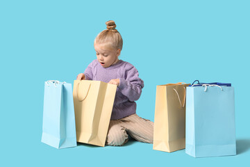 Wall Mural - Cute little shocked girl in warm stylish sweater with shopping bags sitting on blue background