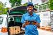 © unai - African young courier using digital tablet to deliver packages
