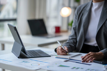 Wall Mural - Businesswoman analyzing financial charts and taking notes in modern office