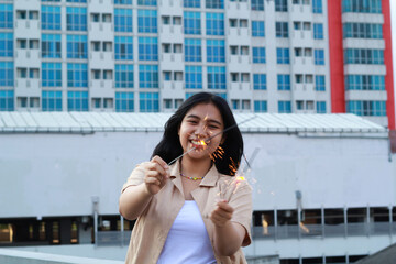 carefree asian young woman holding sparkler celebrate new year eve with laugh and dance in rooftop apartment outdoor with city building background