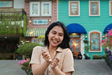 cheerful young asian woman holding sparkler to celebrate new year eve with garden party standing over colorful vintage house yard