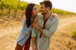© BGStock72 - A joyful couple laughing together in a sunlit vineyard during a warm afternoon, surrounded by lush grapevines and a rustic path