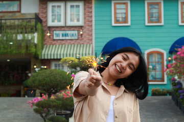 happy young asian woman holding sparkler enjoy new year eve celebration in outdoor garden of colorful vintage house in evening