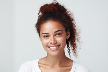 A young woman with curly hair smiles brightly at the camera, exuding happiness and confidence, set against a clean, minimal background.