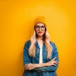 © Eugen Thome - Eine hübsche blonde Hipsterin mit Brille mit gelber Mütze vor einer gelben Wand.