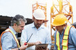 © amorn - Team of male engineer construction using digital tablet for discussing of structure of building at construction site. Group of male construction builder working at construction site