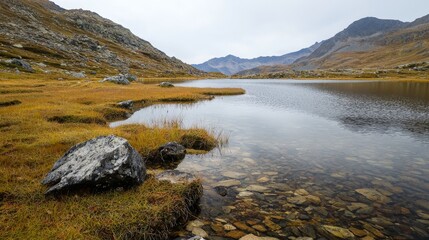  A expansive body of water encircled by grass, featuring a rocky shore dotted with boulders, and distant mountains