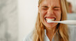 © Yaroslav Astakhov - A young woman intensely brushes her teeth with an electric toothbrush, showcasing her morning routine.