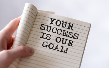 Your success is our goal text on blank business card being held by a woman's hand with blurred background. Business concept to help customers to achieve their goals.