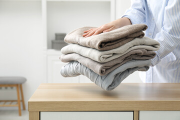 Sticker - Woman with stack of clean clothes near wooden dresser indoors, closeup