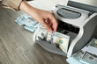 © New Africa - Woman using money counter machine at wooden table, closeup