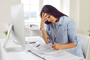 Portrait of a tired young exhausted overworked business woman accountant suffering from headache or eyestrain after long hours computer work sitting at the desk on her workplace in office.