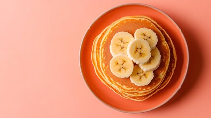 Wall Mural - Golden pancakes with slices of banana on top, placed on a bright coral background, styled with a modern aesthetic