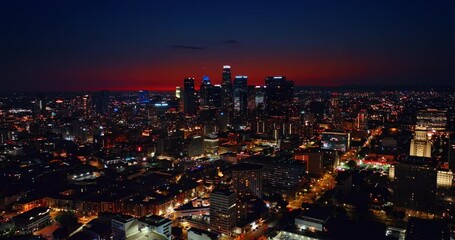 Wall Mural - Skyscrapers of night Los Angeles with neon illumination on tops. Red sky above the metropolis. Drone flying over the city with bright lights.