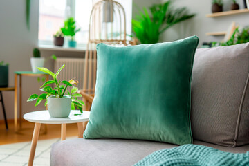 Cozy living room with a green velvet pillow on a grey sofa and potted plants on a side table