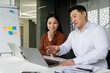 © Liubomir - Asian business professionals engaged in a collaborative project meeting. Man and woman discussing strategy and data with laptops, whiteboard, and notes in modern office environment.