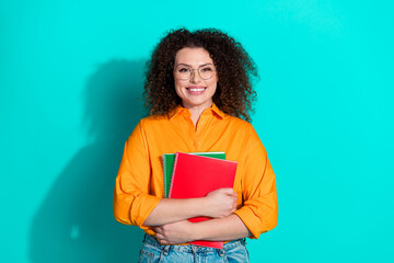 Poster - Photo of smart positive woman with wavy hairstyle dressed orange shirt in glasses cuddle copybooks isolated on teal color background