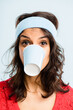 © Moose Coop/peopleimages.com - Funny, crazy and woman with coffee cup in studio for fitness with retro headband for workout. Caffeine addict, goofy and female athlete drinking takeaway cappuccino with vintage exercise fashion.