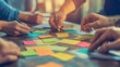 © Your Hand Please - collaborative team working together around a table, hands visible, using sticky notes to brainstorm ideas. The scene emphasizes teamwork, creativity, and problem-solving