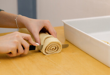 One Caucasian young girl cuts cinnamon dough into pieces on the table.