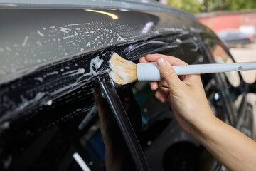 A person is cleaning a car windshield with a brush and water