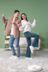 Young couple dancing while modern robot vacuum cleaner cleaning carpet in living room