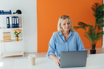 Business woman blonde working with laptop online in white office